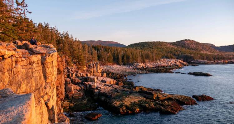 Acantilados dorados y colinas cubiertas de pinos encontrándose con el Océano Atlántico en Acadia durante el atardecer.