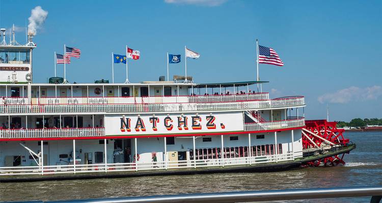 El barco de vapor de paletas Natchez atracó en el río Mississippi con las banderas ondeando al sol.