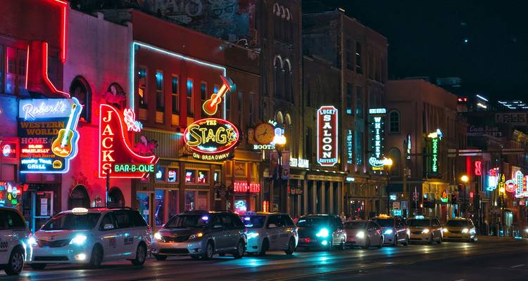 Bares honky-tonk iluminados con neón y tráfico intenso a lo largo de Broadway en Nashville por la noche.