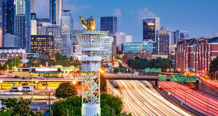 Horizonte de Atlanta al atardecer with torre del pebetero olímpico sobre estelas de luces de la autopista.