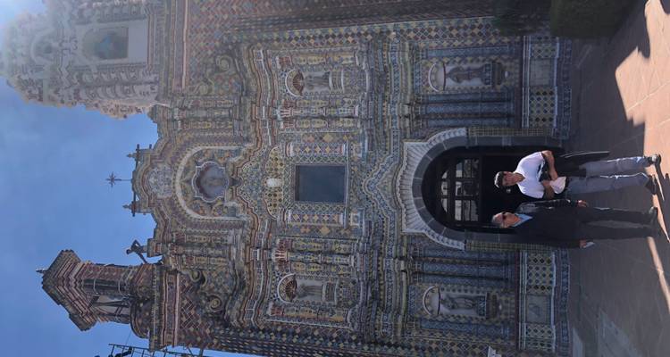 Dos hombres posan frente a la fachada de una iglesia barroca con azulejos intrincados que brilla bajo la luz solar intensa.