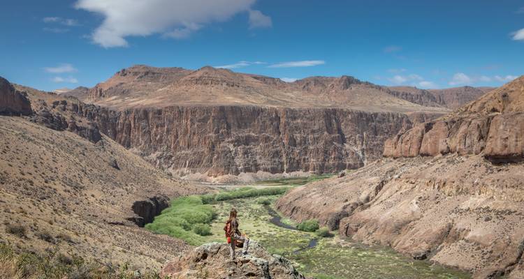 Wandelaar staat bovenop een rotsachtige uitstulping met uitzicht op een dramatische canyon en kronkelende groene rivier.