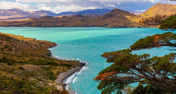 Levendige turquoise meer kronkelt onder windgeteisterde heuvels en verre bergen.