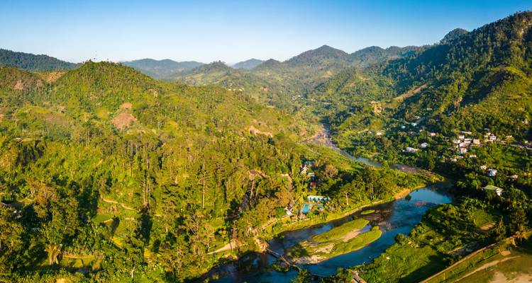 Aerial view of lush green mountains and winding river valley bathed in morning light.
