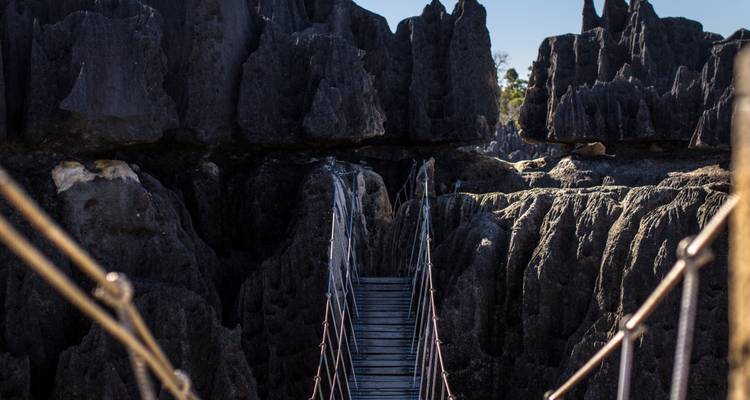 Close-up of a narrow wooden suspension bridge descending into jagged limestone formations.