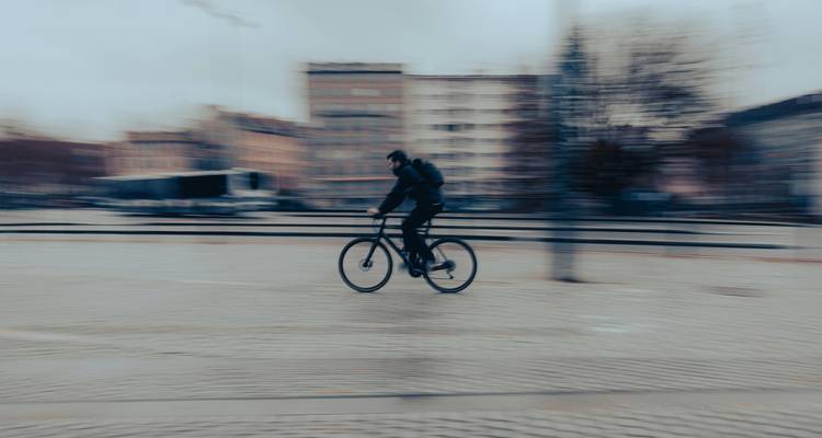 Bewegungsunschärfe-Foto eines Radfahrers, der an einem bewölkten Tag durch einen städtischen Platz fährt.