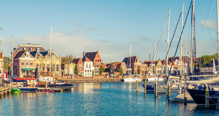 Malerischer niederländischer Hafen, gesäumt von farbenfrohen Giebelhäusern und vertäuten Segelbooten an einem sonnigen Morgen.