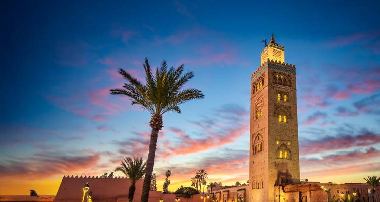 Minarete de la Mezquita Kutubía y una palmera silueteados contra un cielo vibrante de atardecer en Marrakech.