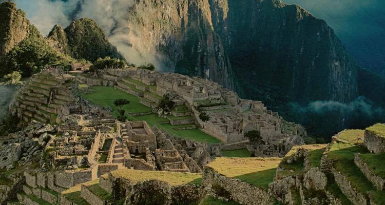 Mistig ochtendgezicht op de stenen terrassen van Machu Picchu en omringende pieken die gedeeltelijk in wolken zijn gehuld.