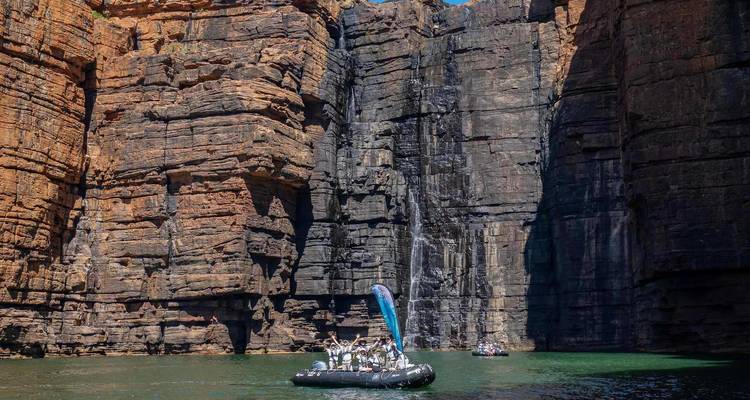 Toeristen in een rubberboot maken een cruise onder imposante rode zandsteenrotsen en een dun watervalhoogtepunt in de Kimberley, Australie.