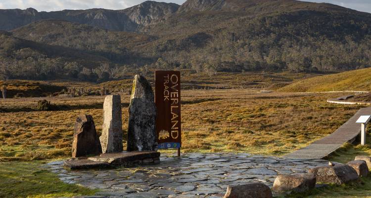 Steinmonument und Schild, die den Beginn des Overland Track markieren, stehen in einem weiten alpinen Moorland.