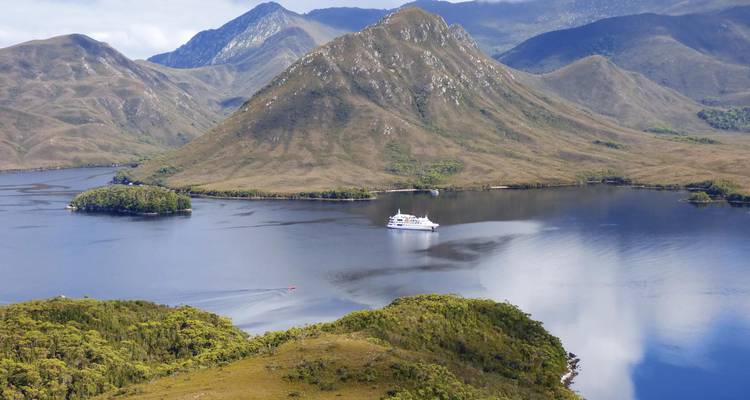 Un pequeño crucero a la deriva en una ensenada remota de Tasmania rodeado de colinas escarpadas.