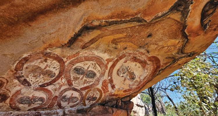 Art rupestre aborigène ancien représentant des figures et des animaux peints sous une corniche de grès surplombante.