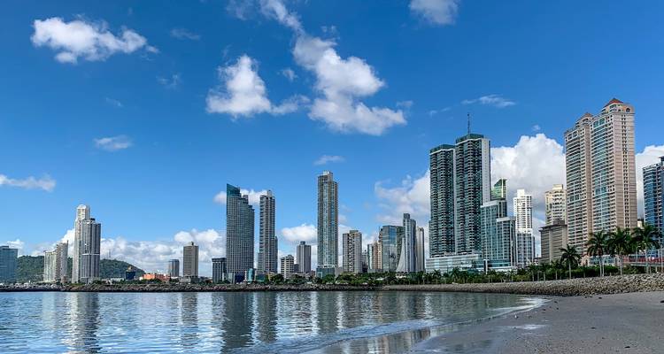 Moderne skyline van Panama-Stad weerspiegeld in kalm kustwater onder een heldere blauwe hemel.