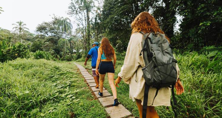 Achteraanzicht van wandelaars die langs een verhard junglepad lopen, waarvan er een een grote rugzak draagt.