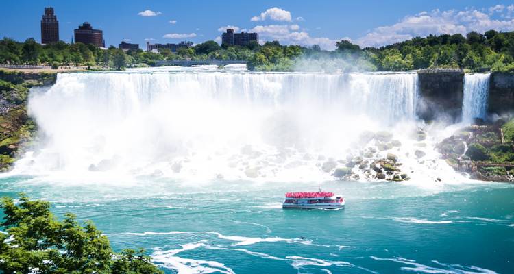 La poderosa cortina de las Cataratas del Niágara ruge hacia el río turquesa mientras un barco turístico se acerca a la neblina.