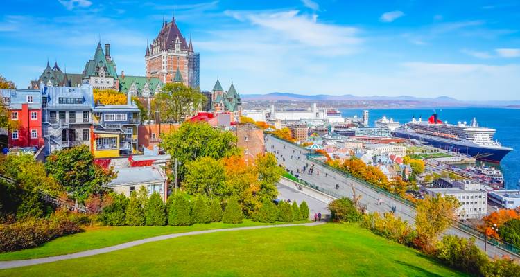 Una vista panorámica colorida del Viejo Quebec con el Château Frontenac elevándose sobre el río San Lorenzo y el follaje otoñal.