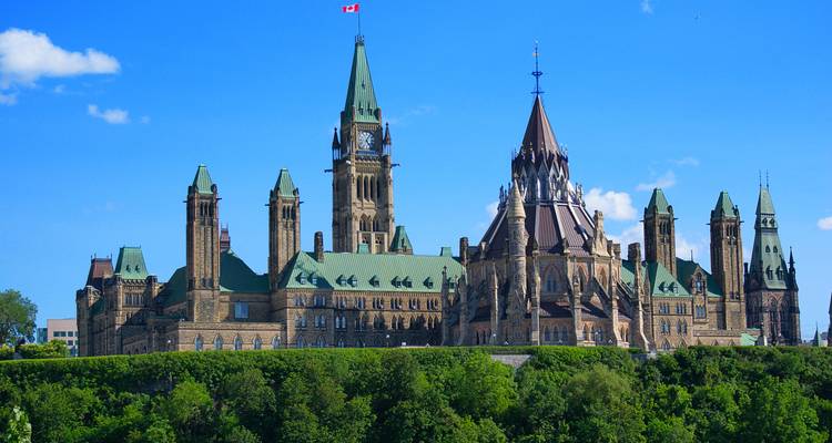 Los Edificios del Parlamento de Canadá se alzan sobre exuberantes árboles verdes contra un cielo azul vívido.