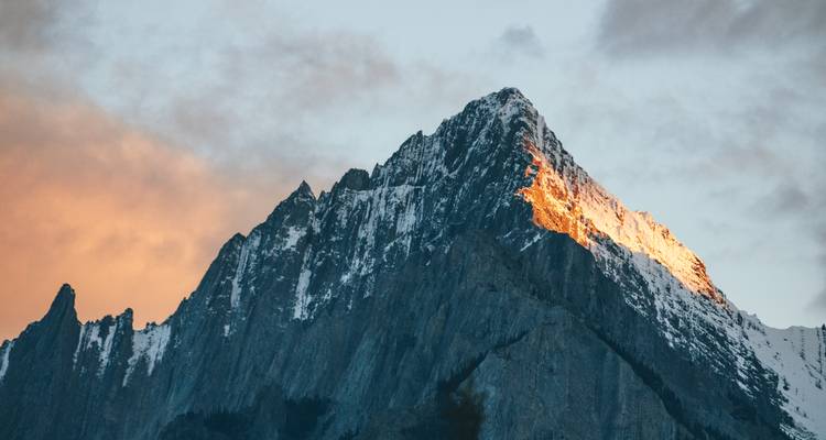 Pic rocheux acéré des Montagnes Rocheuses rougeoyant d'un chaud éclat alpin contre un ciel dramatique.