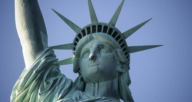 Vue rapprochée en contre-plongée du visage et de la couronne de la Statue de la Liberté sur un ciel dégagé.
