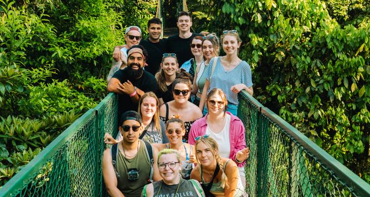 Un groupe de touristes souriants pose ensemble sur un étroit pont suspendu au milieu d'un feuillage luxuriant de forêt tropicale.