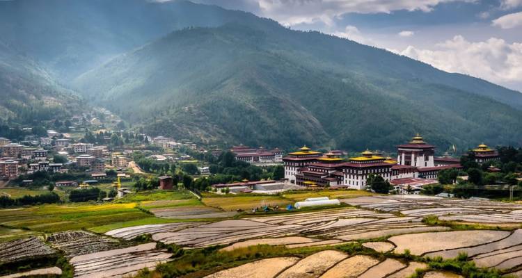 Wiederholte Panoramaansicht von Thimphu mit Dzongs und Reisterrassen unter dunsigen Bergen.