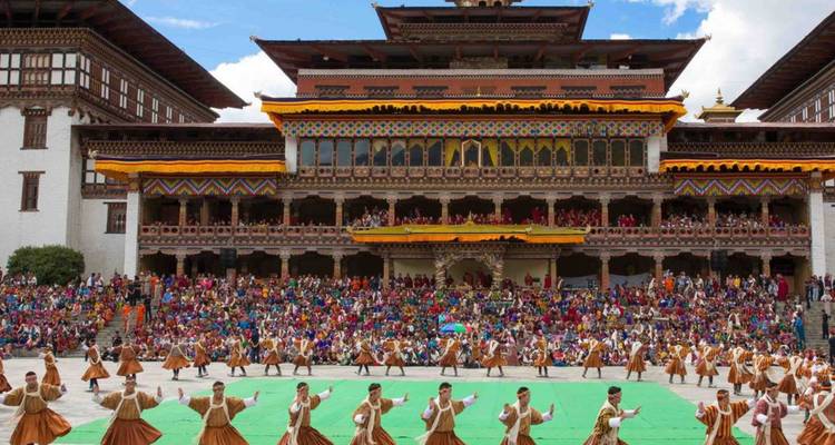 Farbenfroher Freiluftfest an einem bhutanischen Dzong mit Tänzern, die vor einem großen Publikum auftreten.