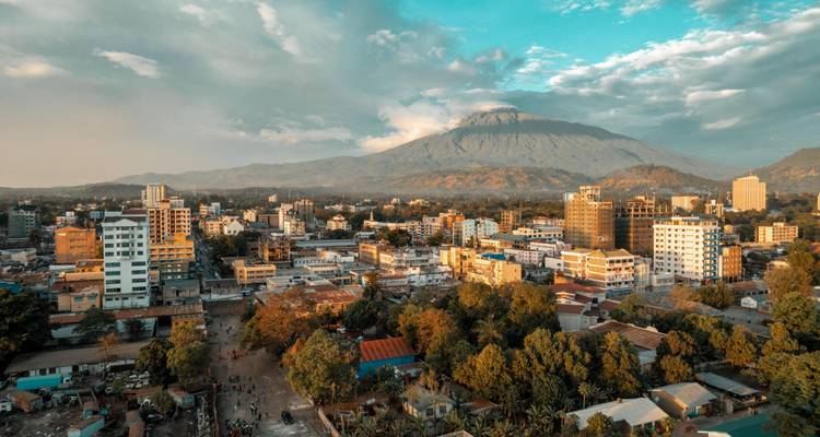 Vue aérienne du paysage urbain d'Arusha avec des bâtiments modernes et le mont Meru en arrière-plan éclairé par une lumière chaleureuse.