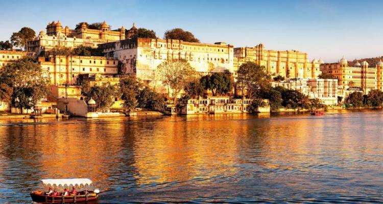 Lumière dorée se reflétant sur le Palais de la Ville d'Udaipur avec un petit bateau sur le lac au coucher du soleil