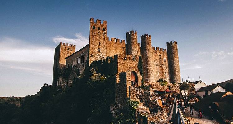 Castillo de piedra medieval con múltiples torres almenadas encaramado en una colina rocosa.