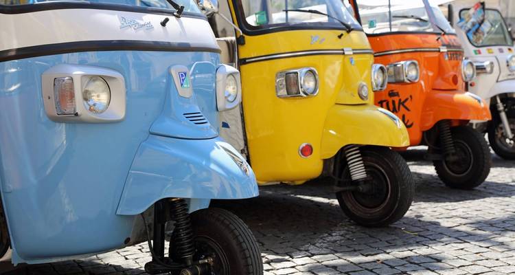 Fila de frentes de tuk-tuk coloridos alineados en calle empedrada.