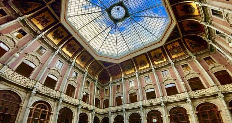 Gran atrio octagonal con cúpula de vidrio y balcones ornamentados dentro de un edificio histórico.