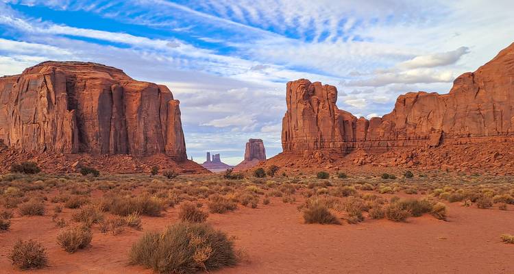 Uitgestrekte rode woestijnvlakte omlijst door torenhoge zandstenen buttes onder een gepatrooneerde hemel in Monument Valley.