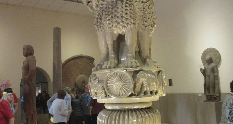 Exposition de musée intérieure du Chapiteau aux Lions d'Ashoka avec des visiteurs observant la sculpture ornée du pilier.