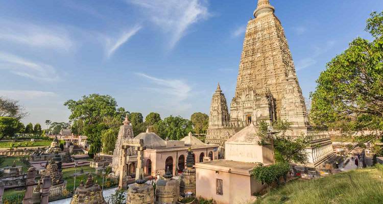 Majestueux temple Mahabodhi s'élevant au-dessus des sanctuaires environnants et des pelouses vertes sous un ciel bleu dégagé.