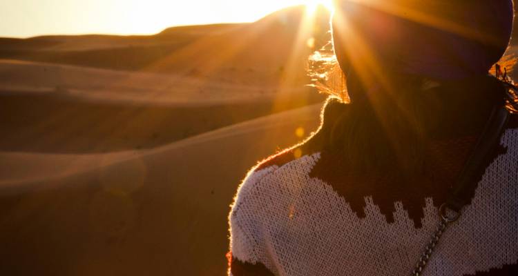 Voyageur en silhouette enveloppé dans une écharpe regardant les rayons du lever de soleil sur les dunes du Sahara.