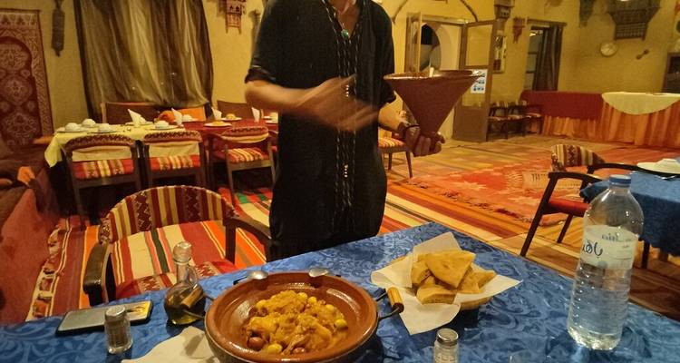 Un hôte présente un tajine marocain traditionnel sur une table de restaurant chaleureusement éclairée avec du pain et de l'eau en bouteille.