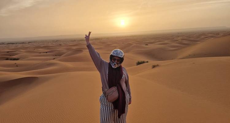 Voyageur casqué fait un signe de paix au sommet d'une vaste dune tandis que le soleil se couche sur le sable ondulant.