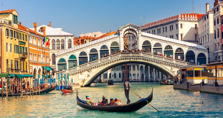 Gondel mit Passagieren, die bei hellem Sonnenschein unter der Rialtobrücke am Canal Grande hindurchfährt.