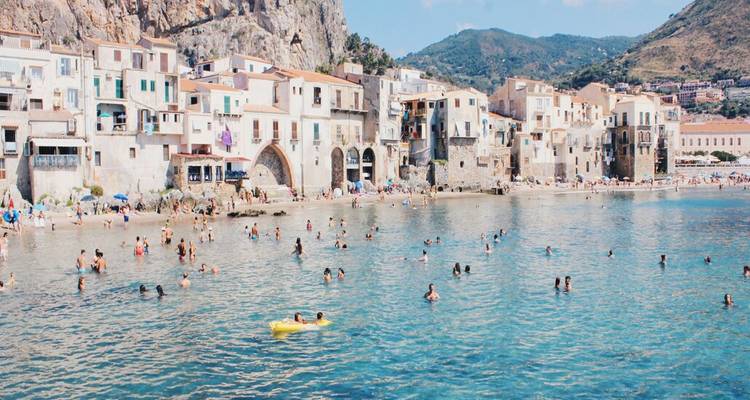 Überfüllte türkisfarbene Bucht mit Schwimmern, die das Wasser vor weißen Häusern am Meer genießen.
