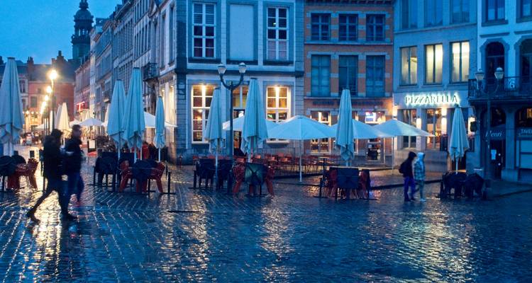 Place pavée de pavés mouillés de pluie, bordée de bâtiments historiques et de cafés au crépuscule, parapluies fermés.