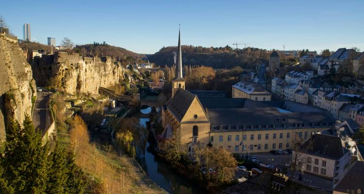 Vue panoramique sur les anciens quartiers de la Ville de Luxembourg avec clocher d'église, falaises et vallée fluviale sinueuse.