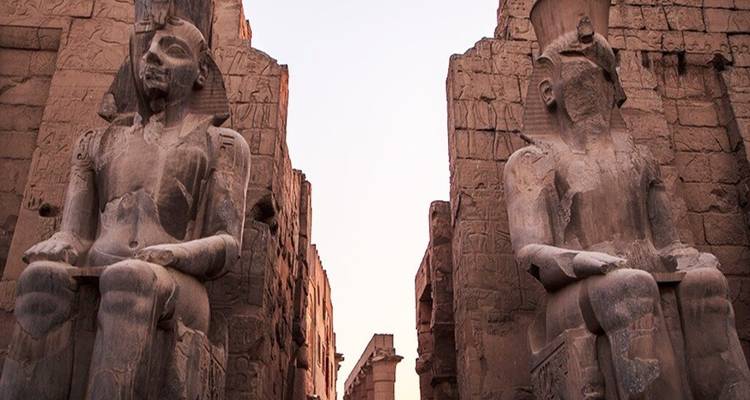 Kolossale zittende beelden bewaken de ingang van de Luxor Tempel in zacht schemerlicht.