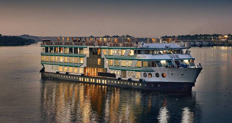 Moderne Nijlcruiseschip verlicht in de schemering weerkaatsend op kalme rivierwateren.