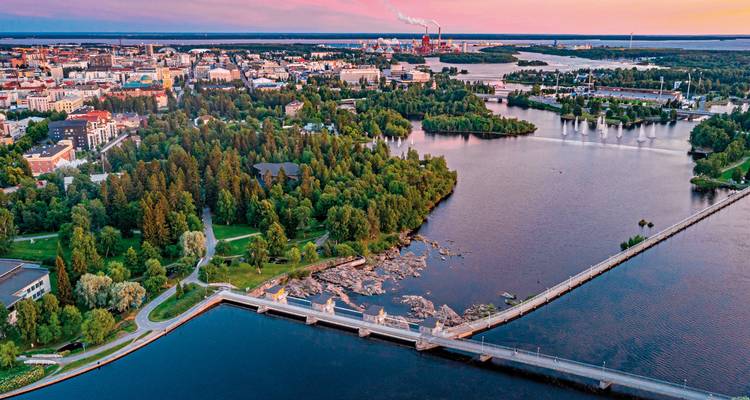 Luftaufnahme einer finnischen Stadt bei Sonnenuntergang mit Parks, Wasserläufen und einer langen Brücke, die in die Innenstadt führt