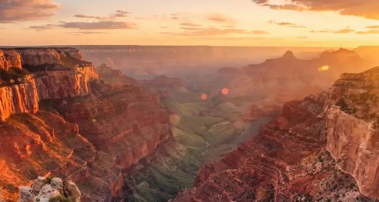 Zonsopganglicht dat de uitgestrekte gelaagde ravijnen van de Grand Canyon overspoelt met gloeiendo rode rotsen.