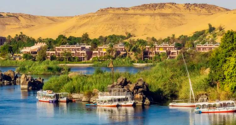 Groene Nijloever met zeilboten en woestijnkam achter luxe resort