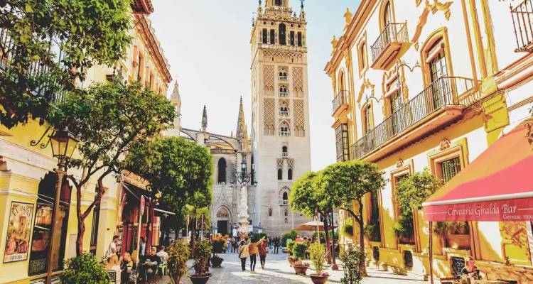 Animada calle peatonal bordeada de edificios naranjas que conduce a la torre Giralda de Sevilla