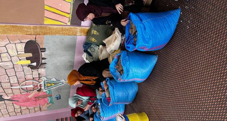Des femmes dans une coopérative sont assises par terre et cassent des noix dans de grands sacs bleus.
