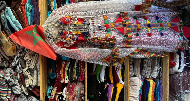 Une robe marocaine traditionnelle colorée sur un mannequin entourée de textiles soigneusement pliés.